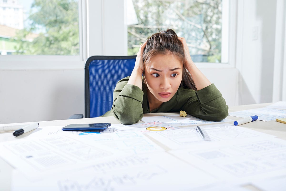 Young woman looking completely overwhelmed while sitting at her work desk.