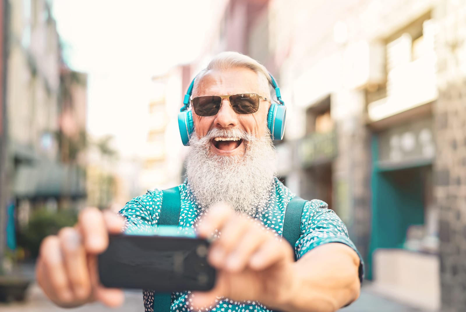Trendy older man laughing while taking a selfie.