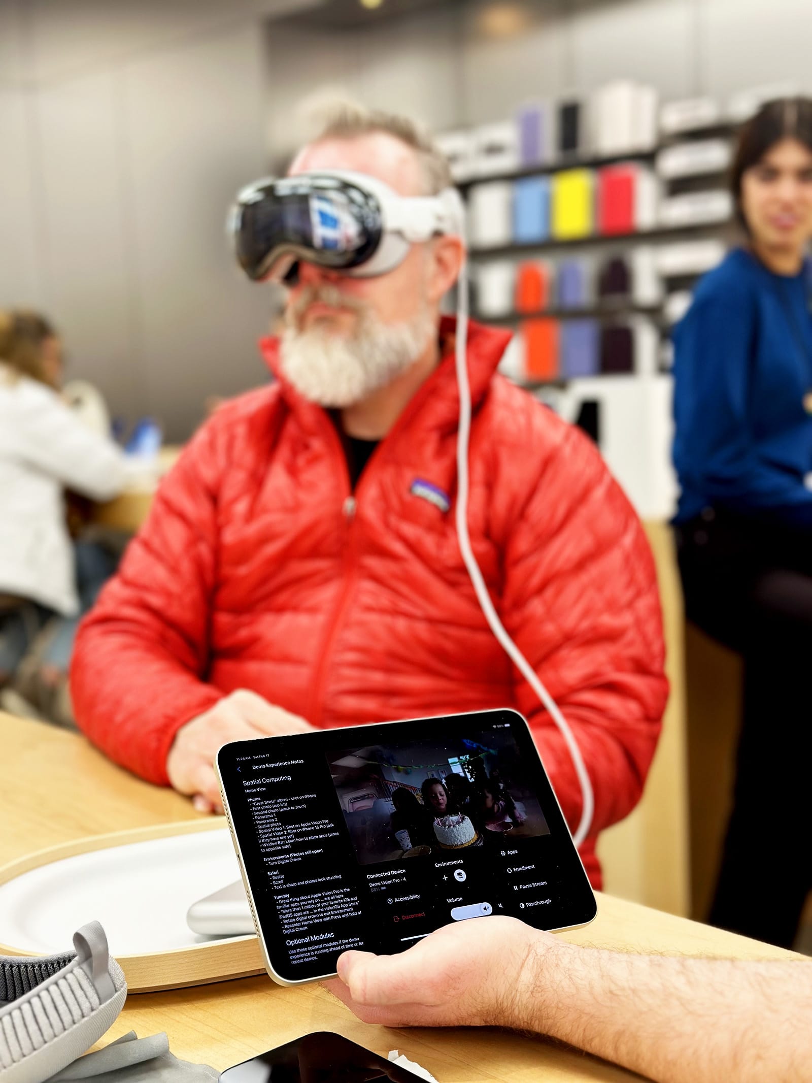 A man holding an iPad running the demo software while another man wears a Vision Pro headset in the background