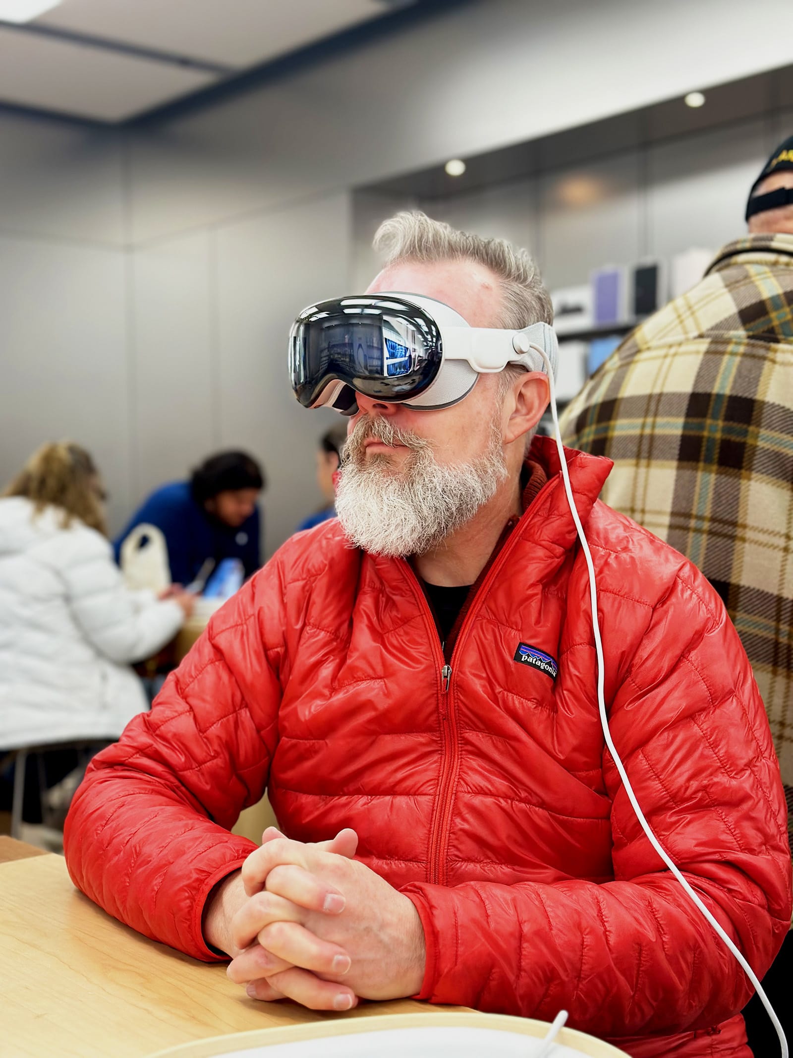 A middle-aged man wearing an Apple Vision Pro headset while seated at a table in an Apple Store.